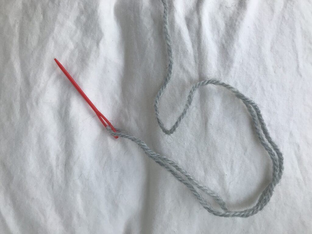 red tapestry needle with grey yarn on a white background