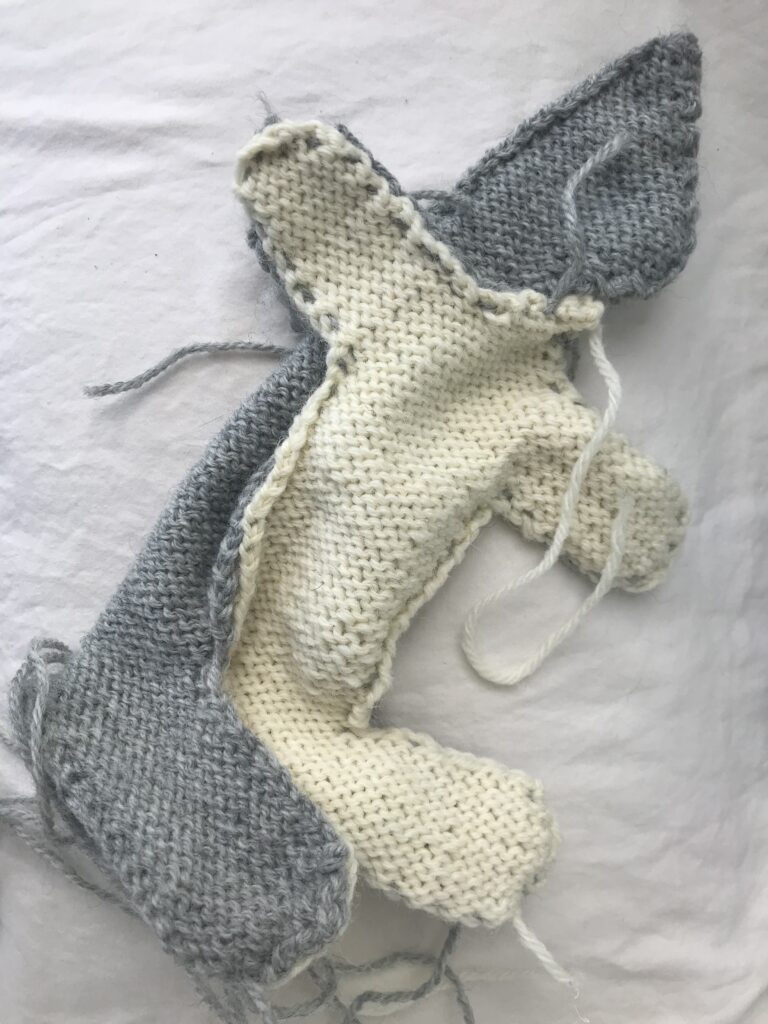 knitted grey and white rabbit body turned inside out being assembled on white background