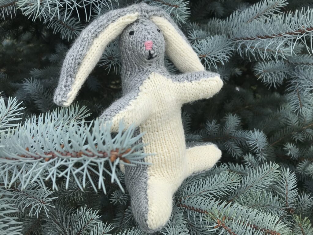 grey and white knit rabbit in a fir tree