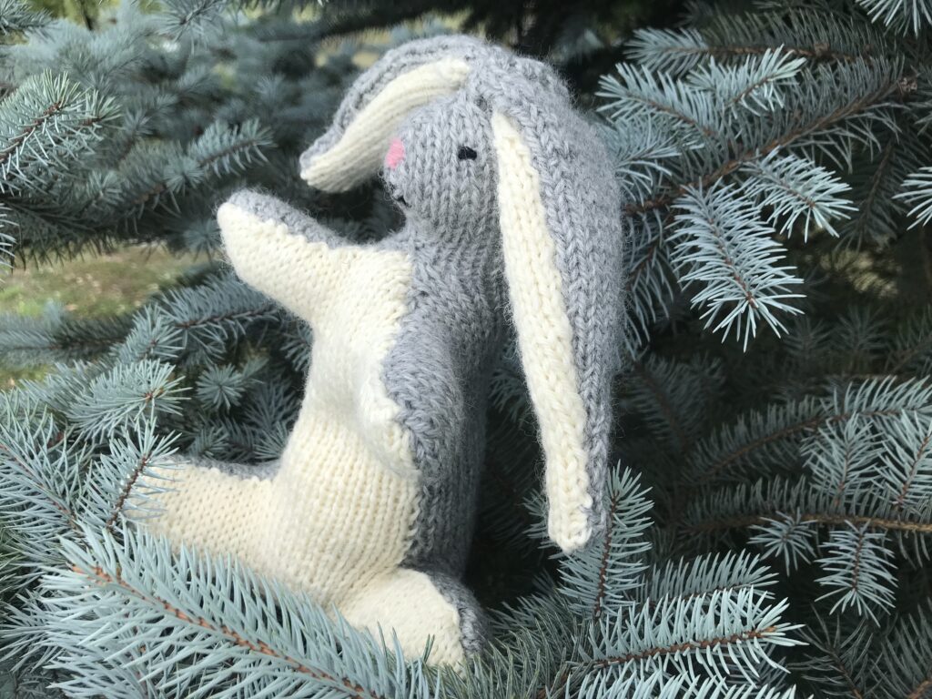 grey and white knitted velveteen rabbit in a Christmas tree