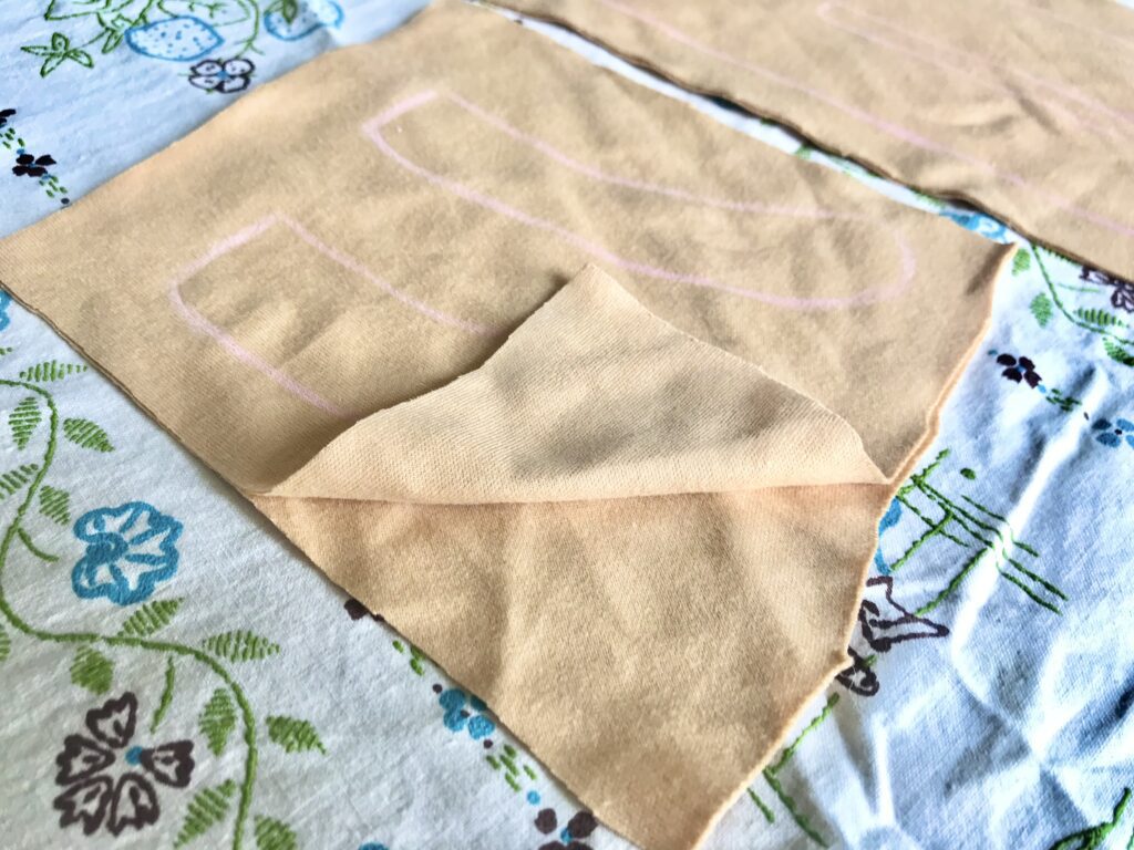 two layers of tan fabric with pink pencil markings traced on it. on an embroidered tablecloth