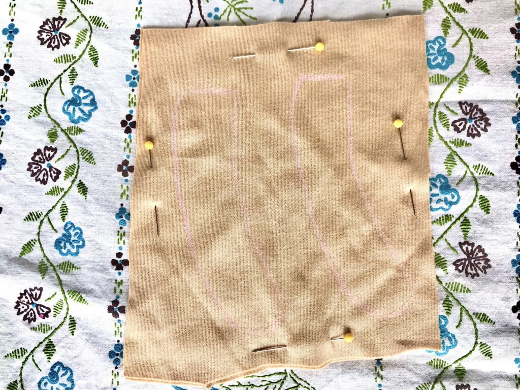 pink penciled markings on tan fabric with yellow pins on a tablecloth