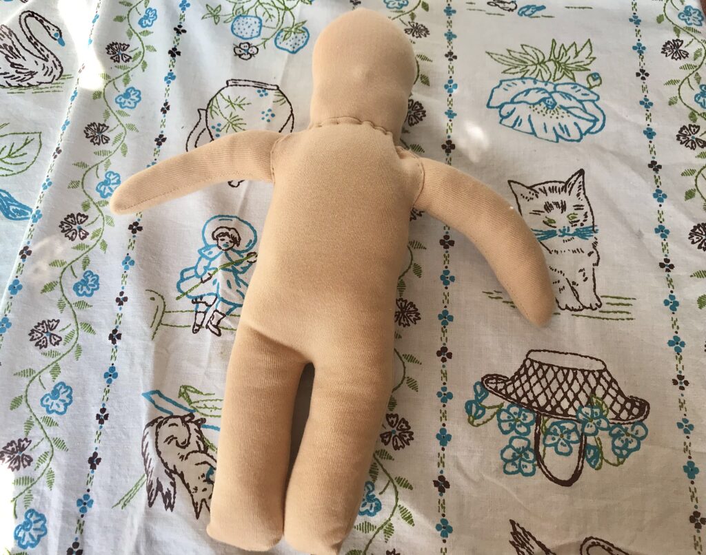 waldorf doll body being sewed together on a colorful tablecloth