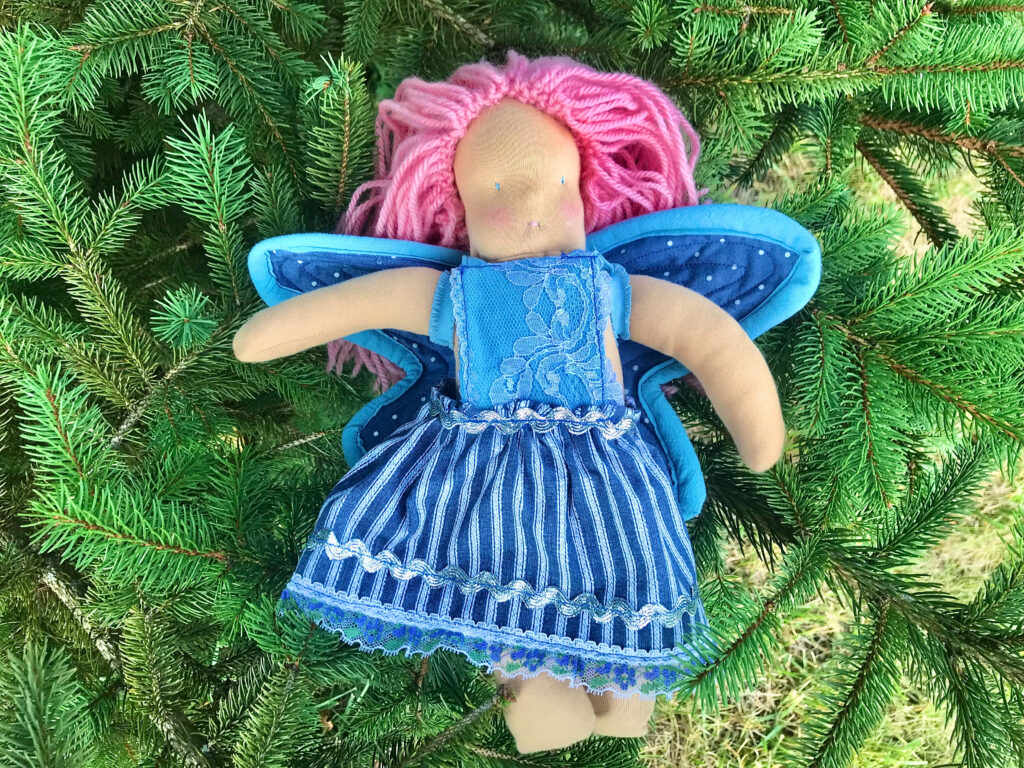 Waldorf Fairy doll with pink hair and blue dress and blue wings on tree 