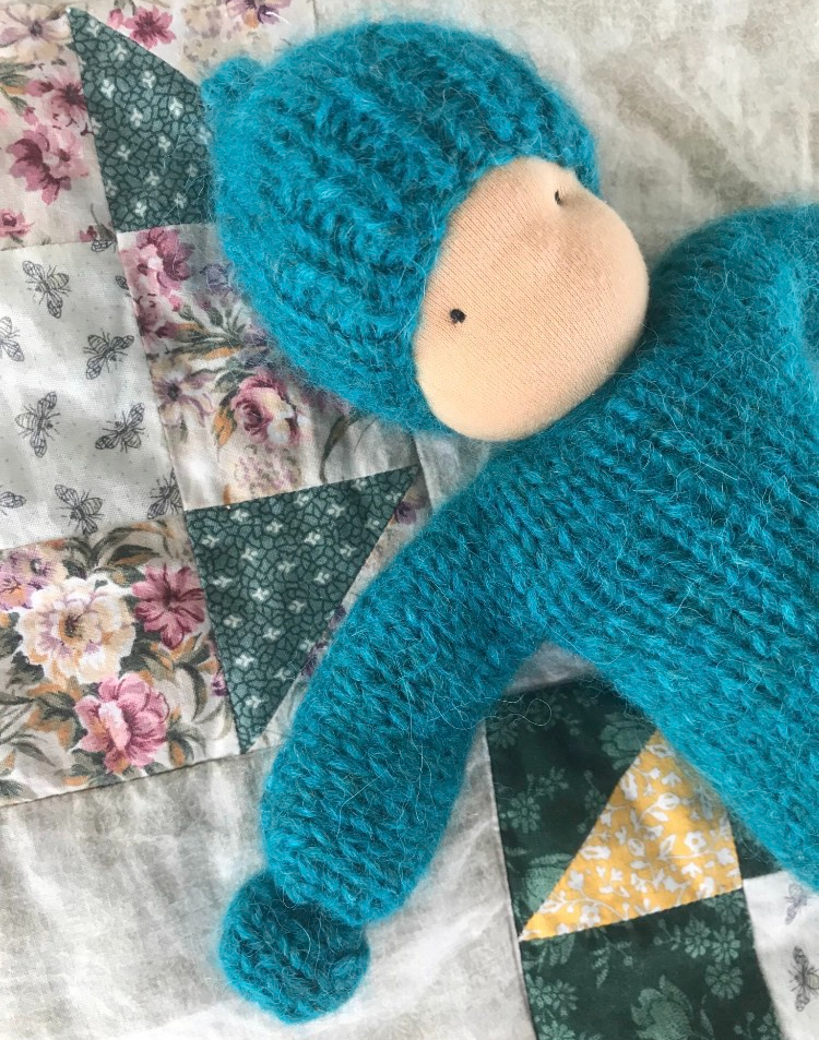 blue knit waldorf doll on a green and yellow and beige quilt