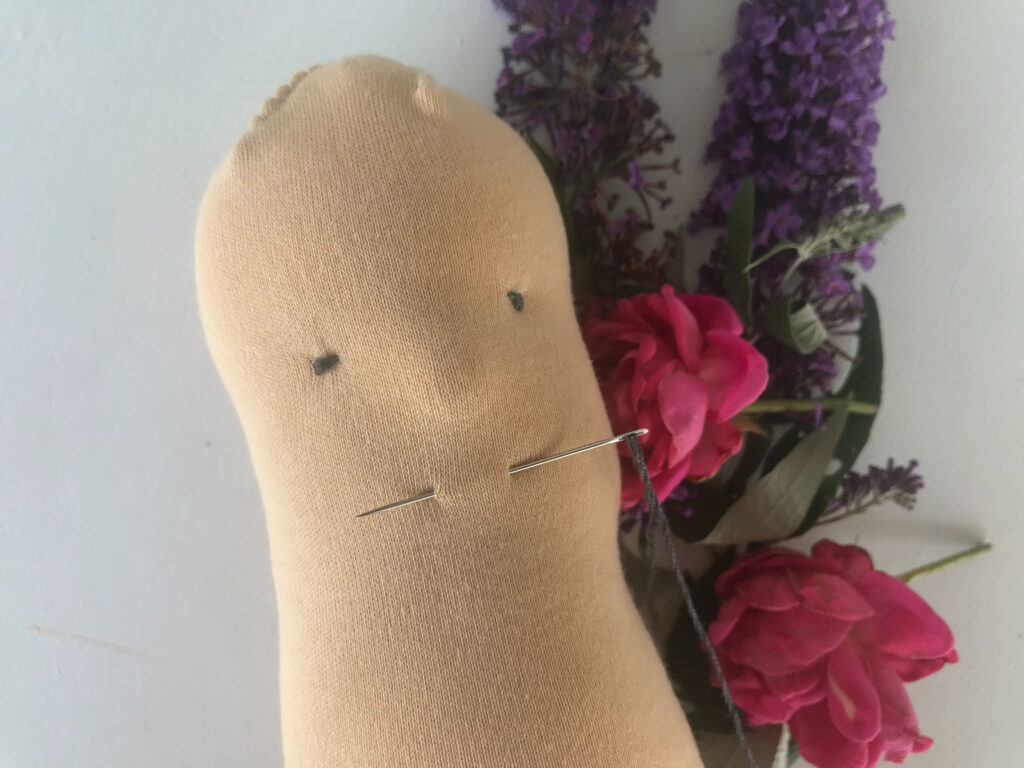 needle sewing mouth on unfinished waldorf doll head with fresh flowers in background
