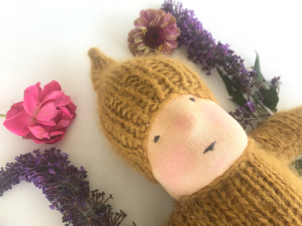 yellow knitted waldorf doll with purple and pink flowers on a white background