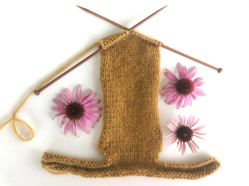 two wooden knitting needles knitting yellow yarn with three pink flowers