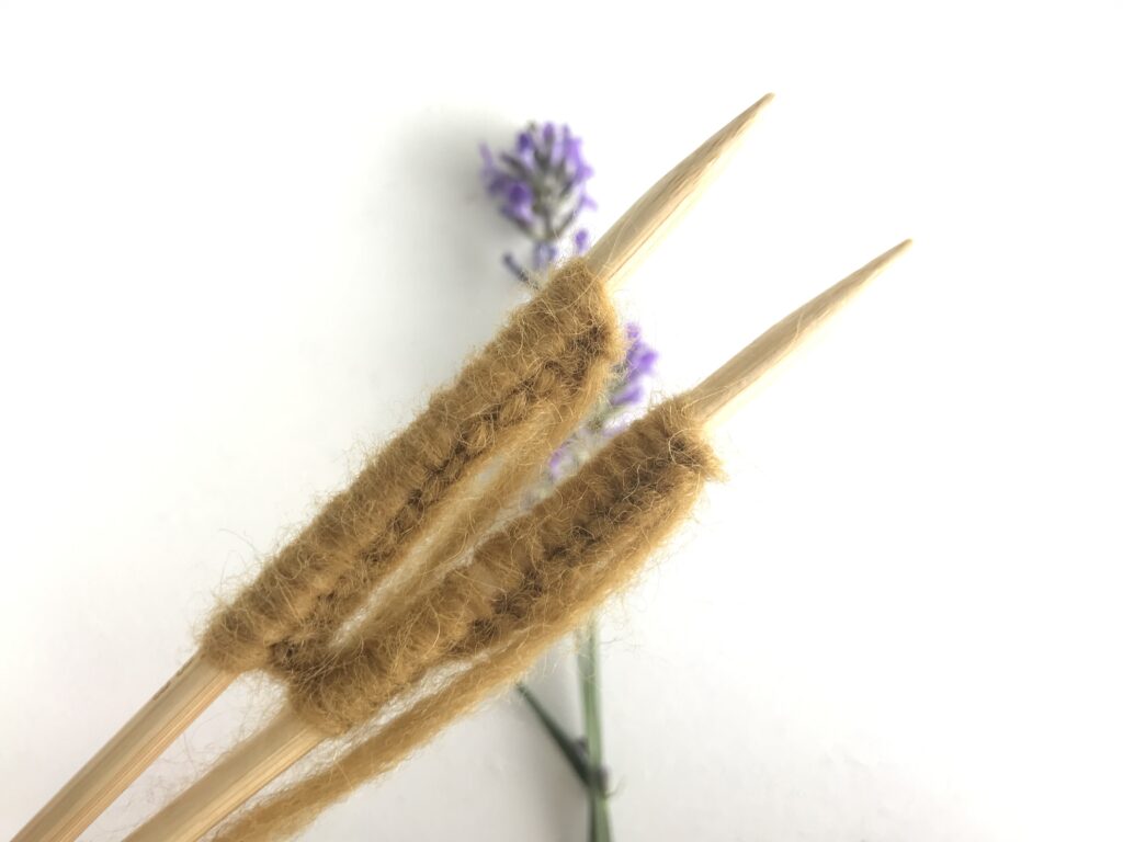 yellow yarn on wooden circular knitting needles with lavender on a white background