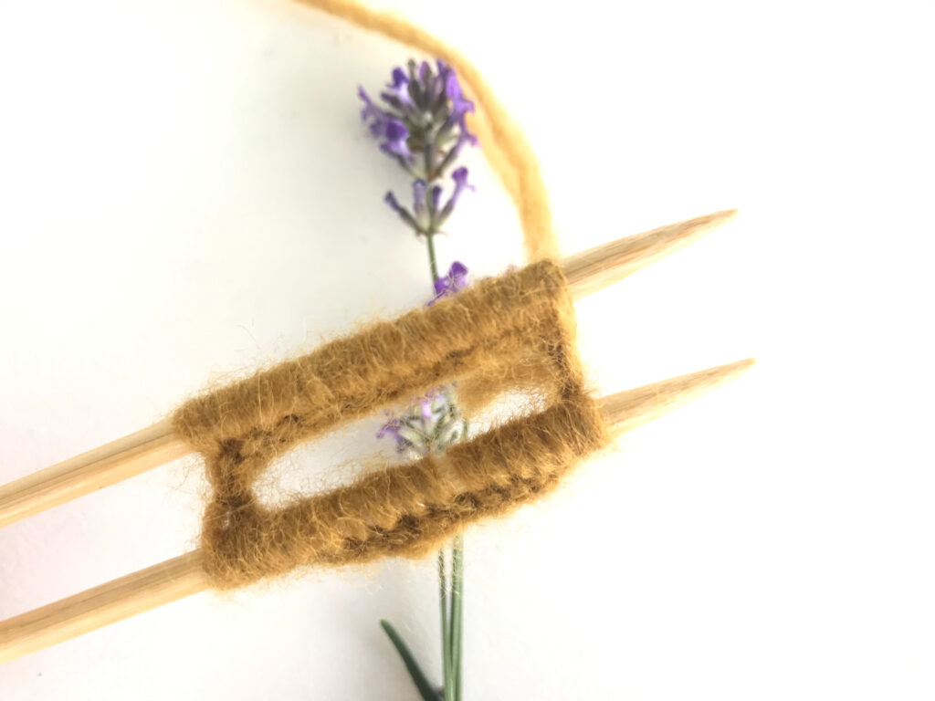 yellow yarn joined on circular needles with lavender on a white background