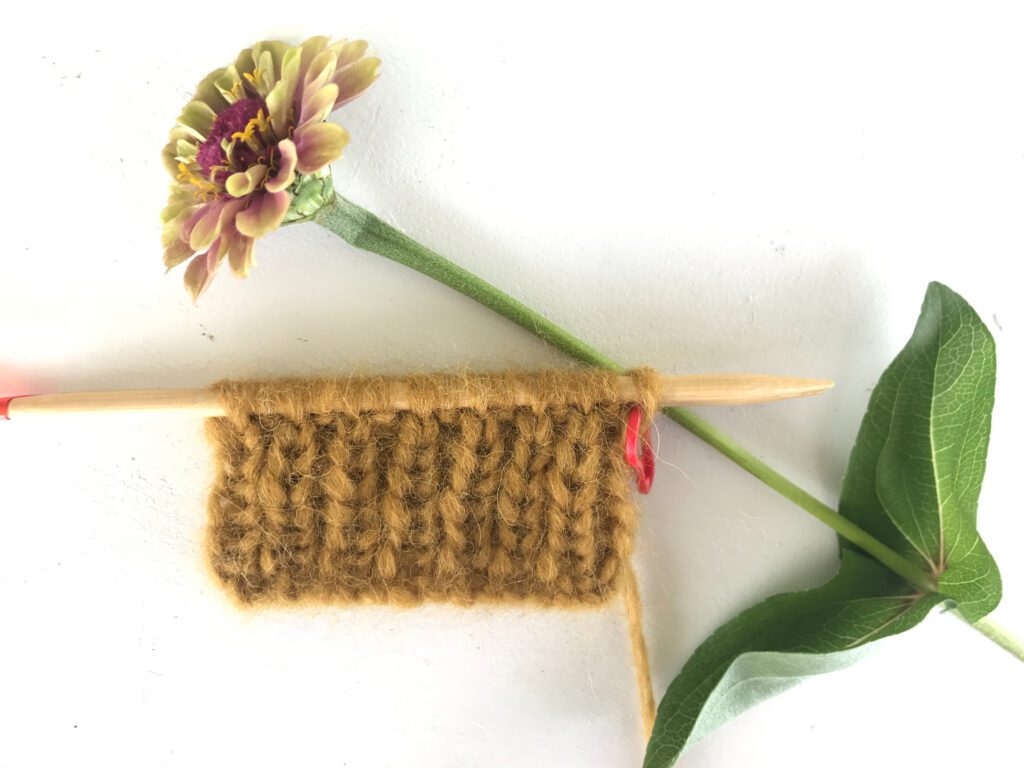 yellow ribbing on circular needles with a red stitch marker and pink flower on a white background