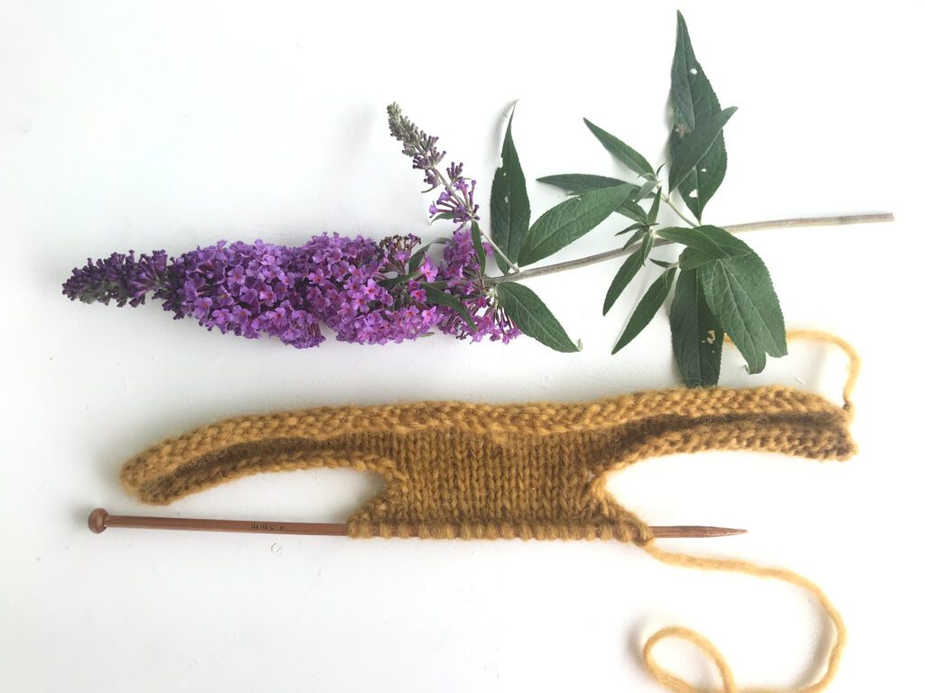 one wooden knitting needle with yellow yarn and a purple flower