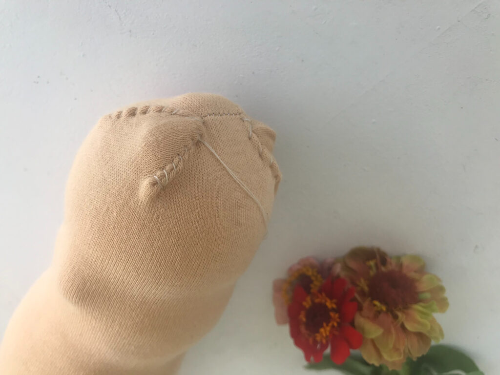 sewing the top of a waldorf doll head with zinnias in background