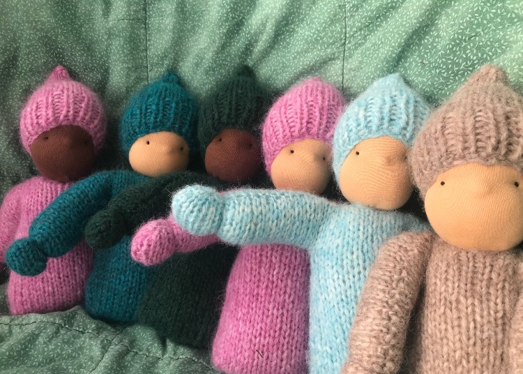 variety of multicolored knitted waldorf doll lined up on a green blanket