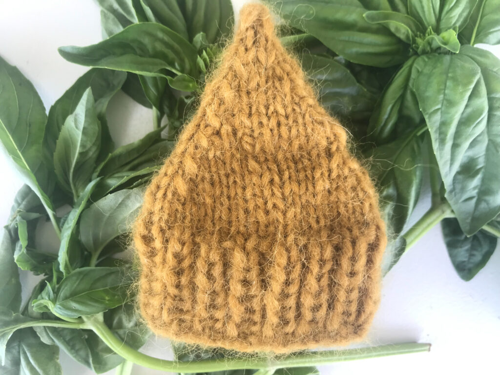 finished yellow waldorf doll hat on some basil on a white background