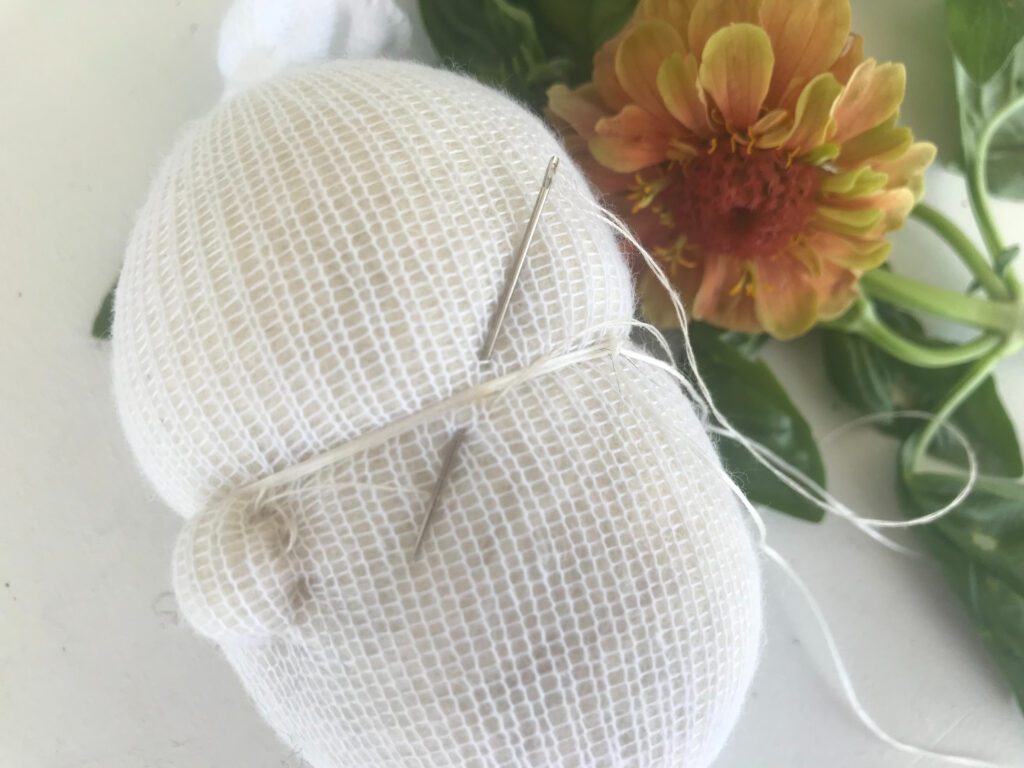 securing the dental floss onto the inner waldorf doll head with zinnia flowers in background