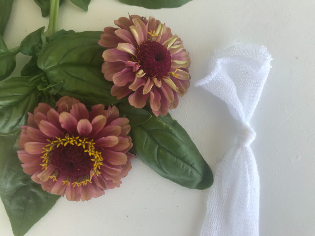cotton gauze tubing tied in a knot on white background with pink zinnias and fresh basil