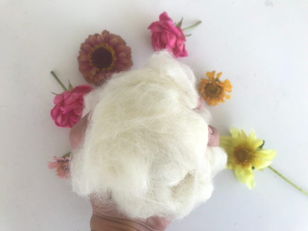 woman's hand holding lambswool with pink, orange, and yellow flowers on a white background