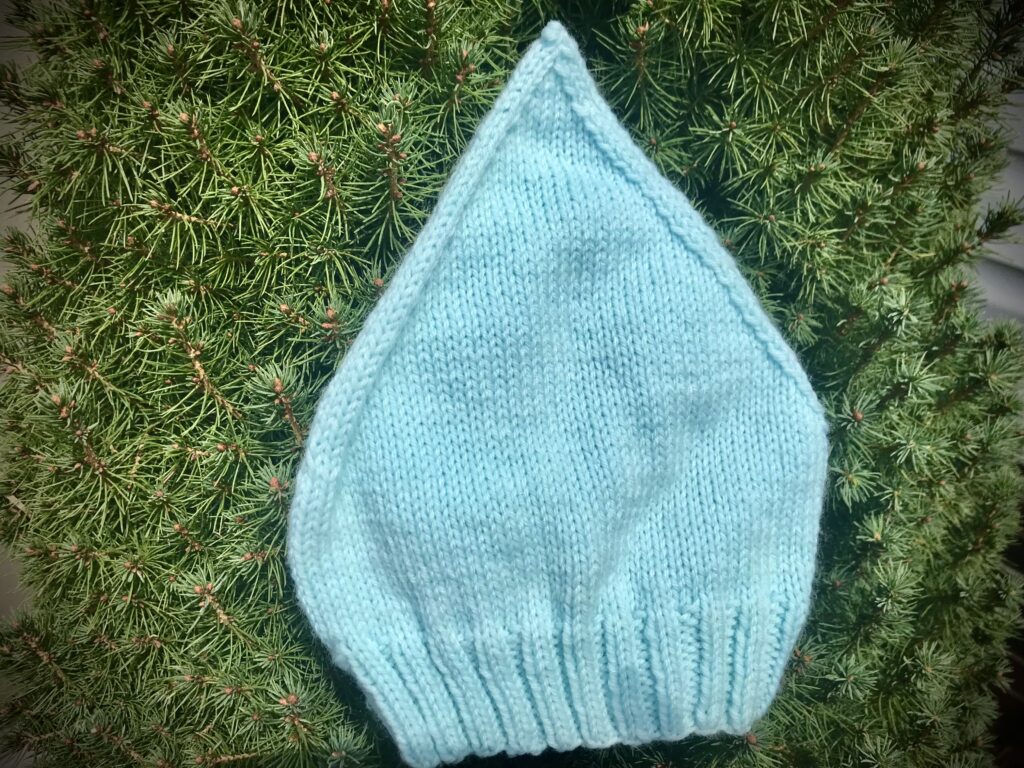 blue knitted baby hat on greenery