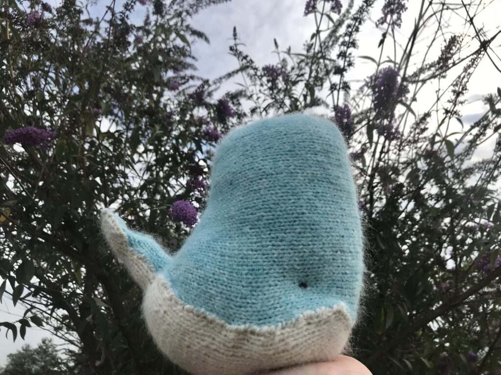 Blue and white knitted whale with butterfly bush and blue sky in background knit whale pattern