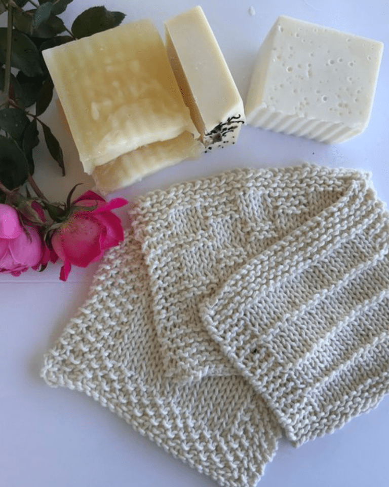 white cotton knitted dishcloths on a white background with homemade soap and pink roses