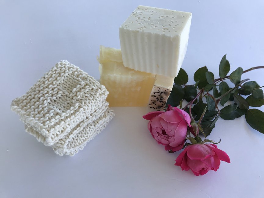 folded white cotton knitted dishcloth on a white background with homemade soap and pink roses