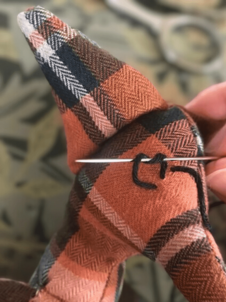 sewing a french knot onto an orange flannel fox doll