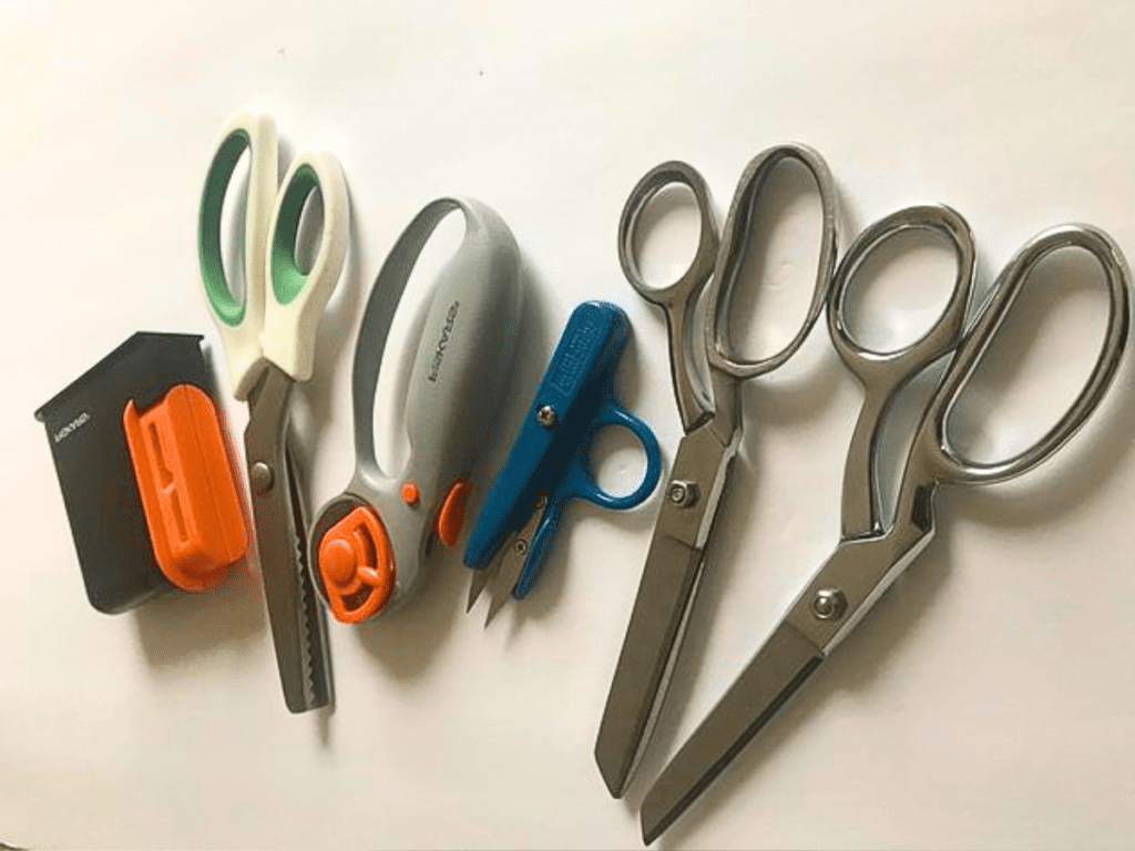 variety of scissors used for sewing and a scissor sharpener on a white background