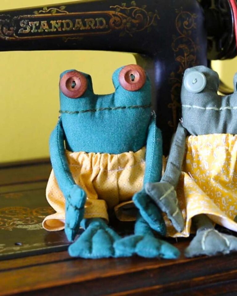 frogs wearing clothes and button eyes sitting in front of an antique treadle sewing machine